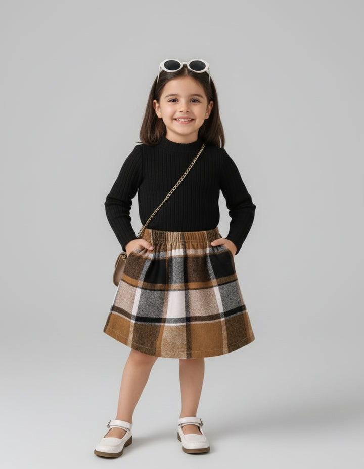 Young girl wearing a black sweater and plaid skirt with sunglasses on her head against a gray background