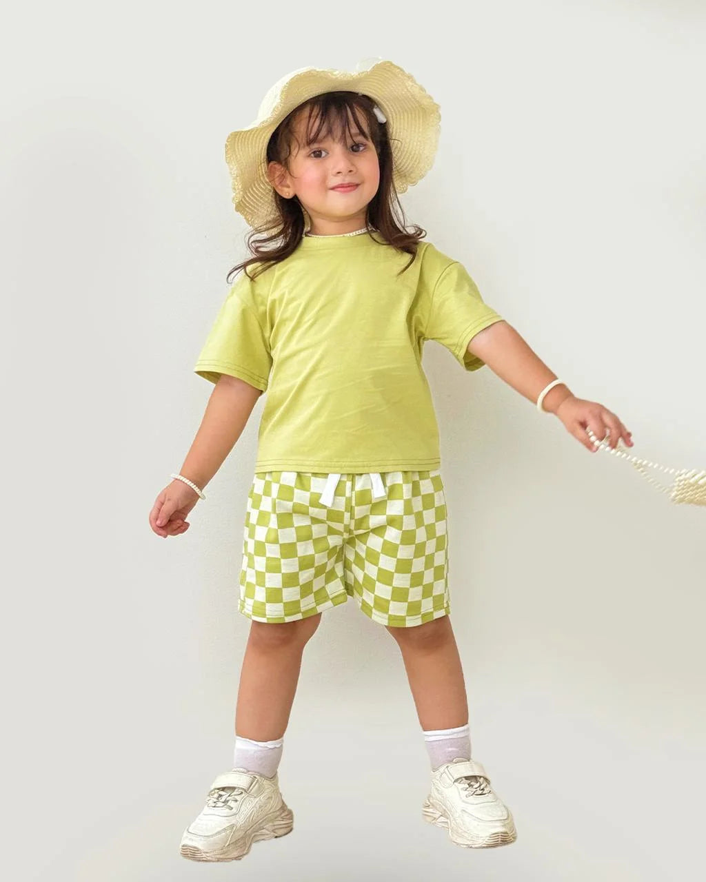 Child wearing a green outfit with a checkered skirt and straw hat on a white background