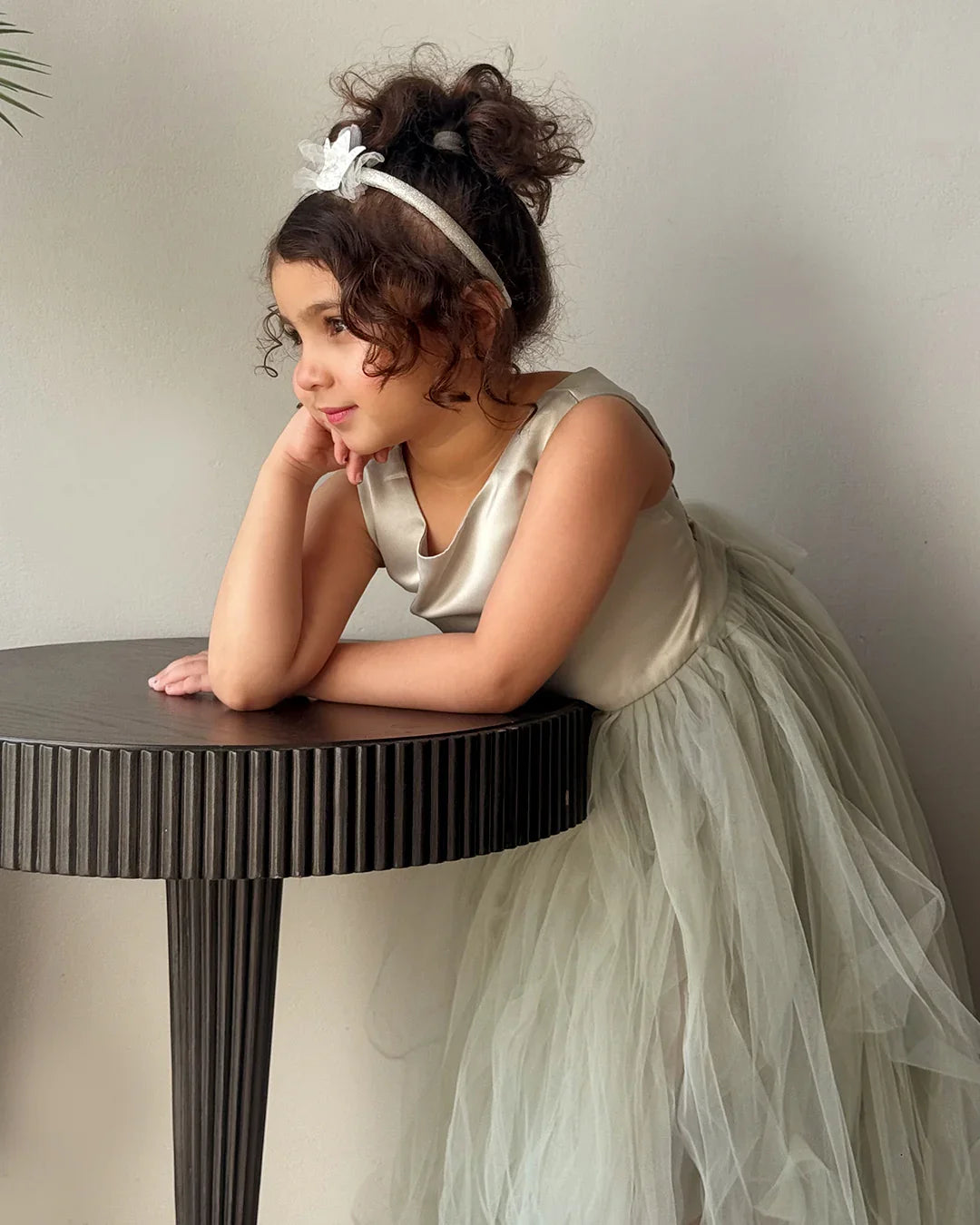 Young girl in a white dress leaning on a table against a plain background