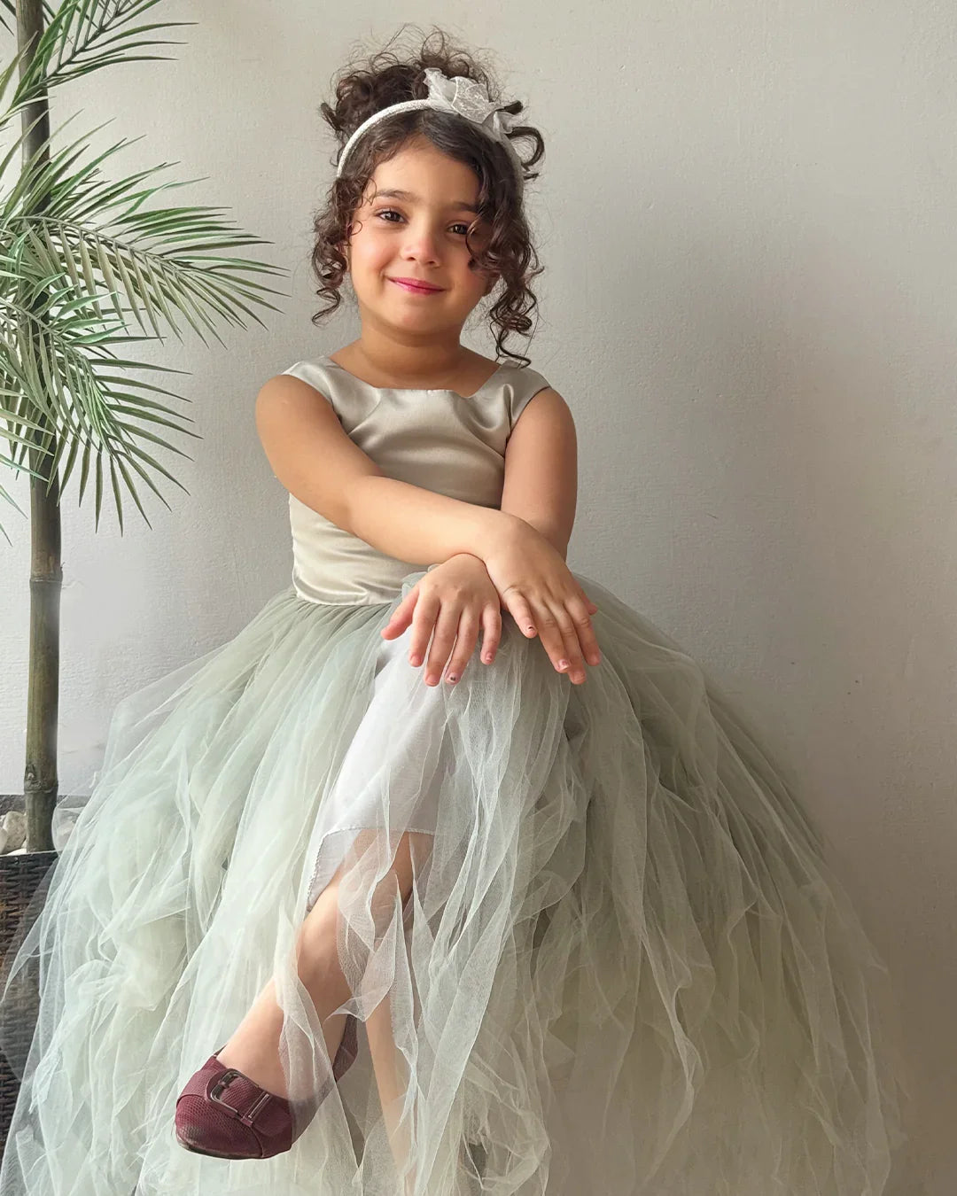 Young girl in a white dress with a tulle skirt sitting indoors.