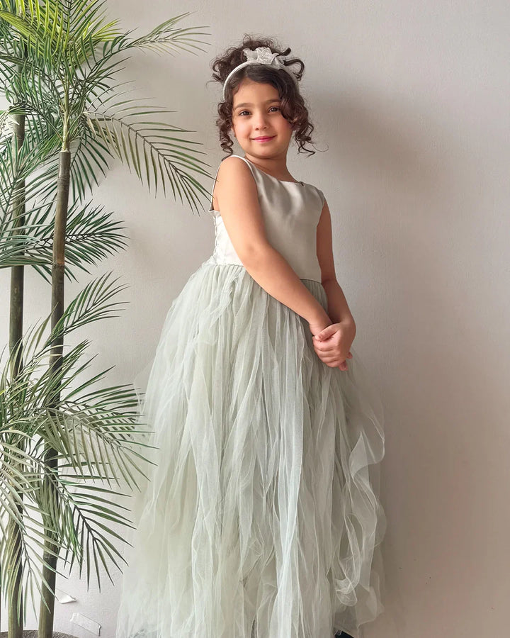 Young girl in a white dress standing next to a plant against a plain wall