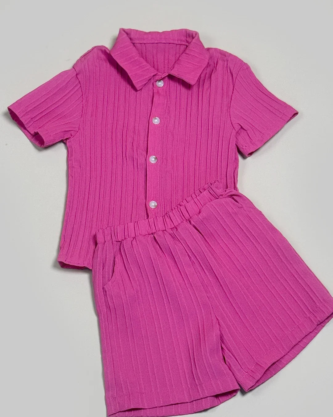 Pink pleated shirt and shorts set on a light gray background