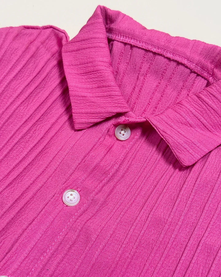 Close-up of a pink textured shirt with buttons on a light gray background