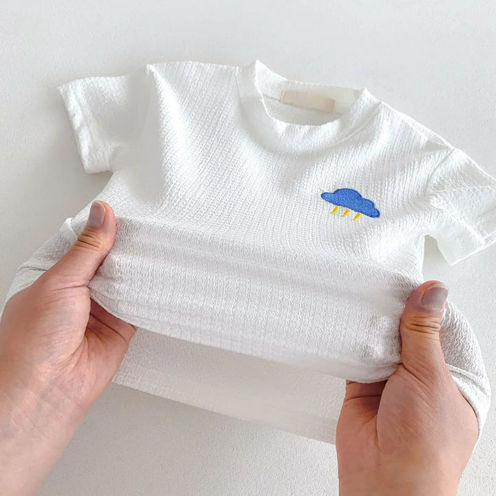White baby t-shirt with a blue cloud design held by hands on a light background