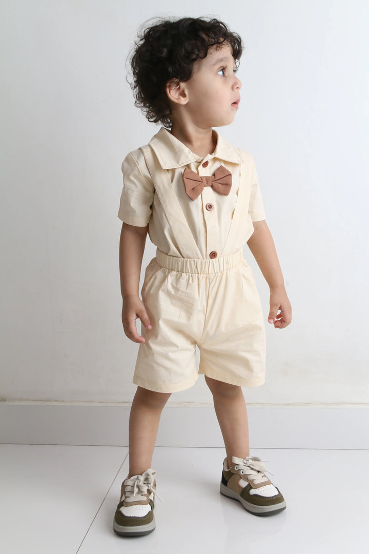 Child wearing a beige outfit with a bow tie on a white floor.