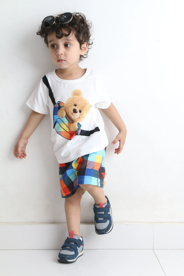 Child wearing a colorful outfit with a teddy bear on a white floor