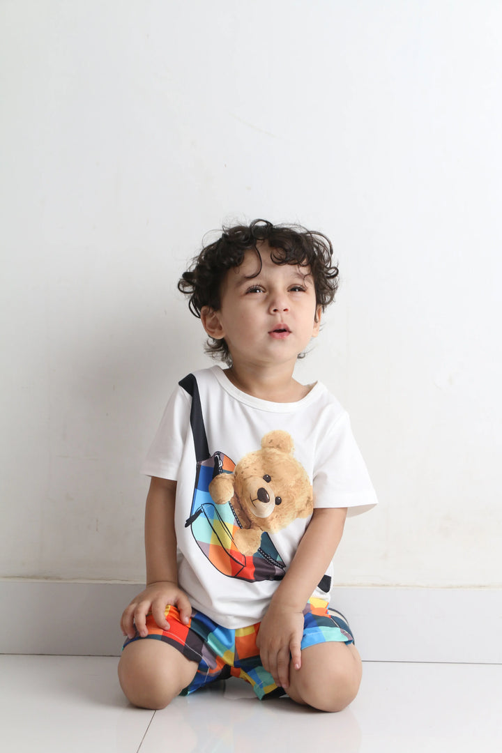 Child wearing a white t-shirt with a colorful design, sitting on a white floor.