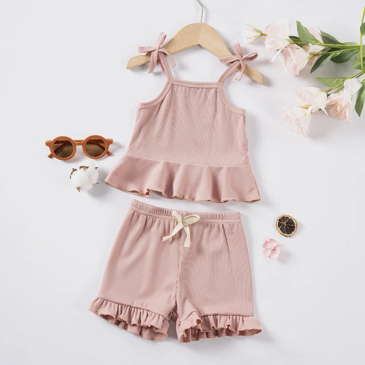 Pink children's outfit with top and shorts on a white background with decorative elements.