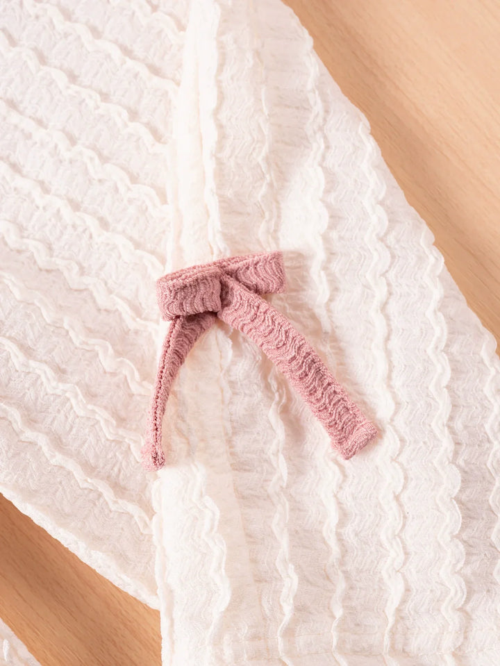 Pink knitted bow on a textured white fabric background