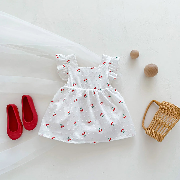 White dress with red cherry pattern, red shoes, and a wicker basket on a white background