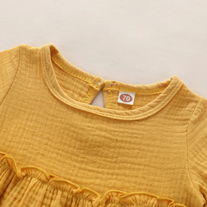 Close-up of a mustard yellow baby dress with a lace collar and label on a beige background