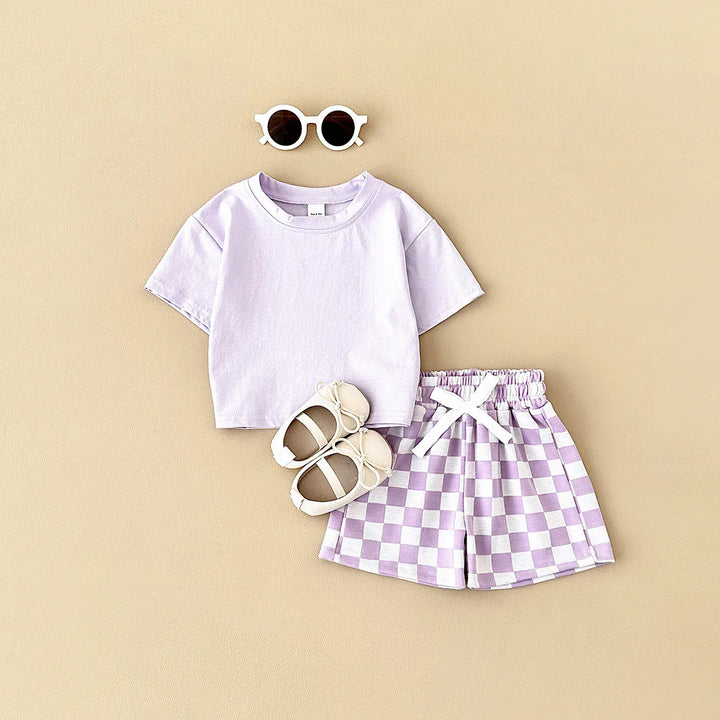 Children's outfit with purple t-shirt and checkered shorts on a beige background