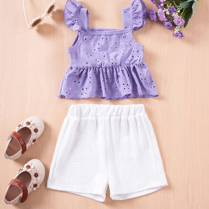 Purple top with ruffled sleeves, white shorts, and shoes on a beige surface with flowers and sunglasses.