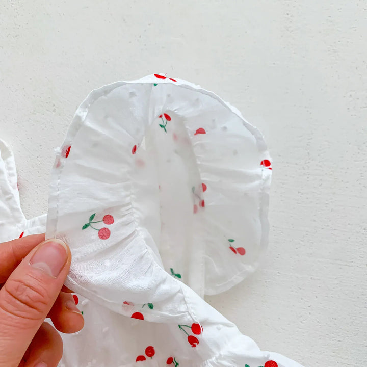White fabric with red cherry patterns held by a hand against a white background