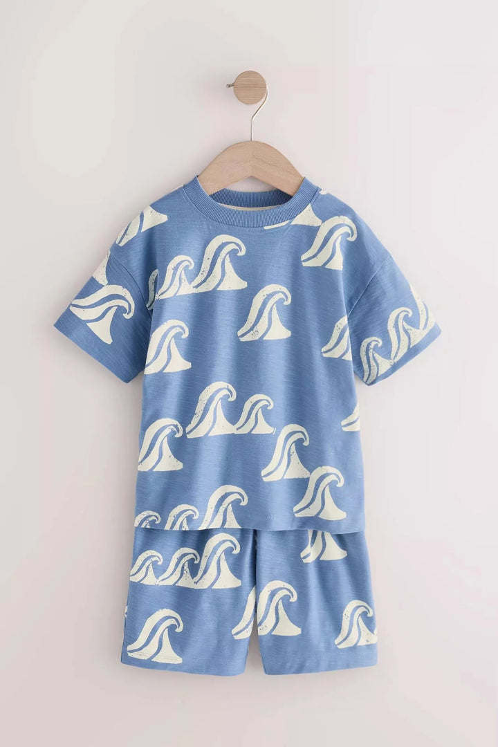 Children's blue pajama set with white wave patterns on a wooden hanger against a light gray background.