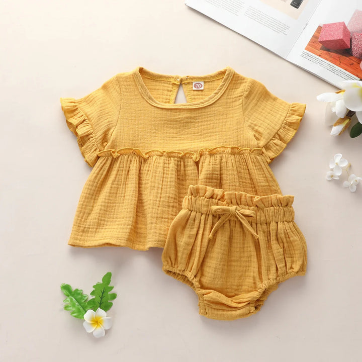Yellow baby dress with ruffled sleeves and matching bloomers on a light background