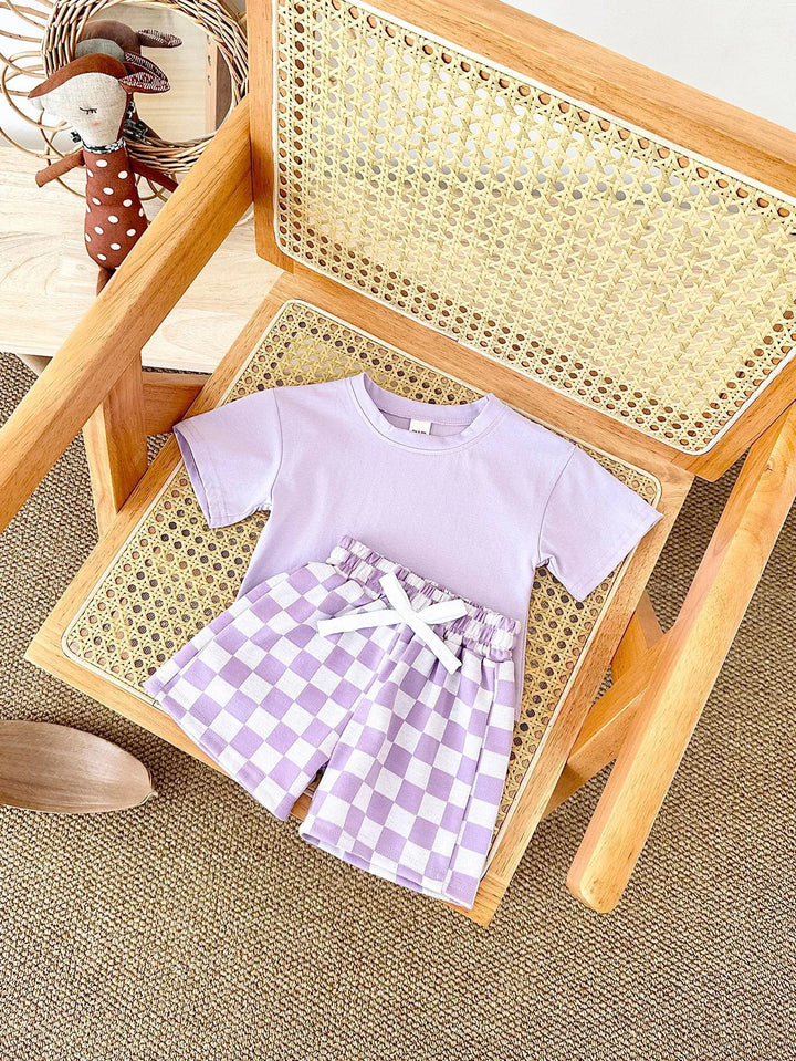 Children's outfit with lavender shirt and checkered shorts on a wooden chair.