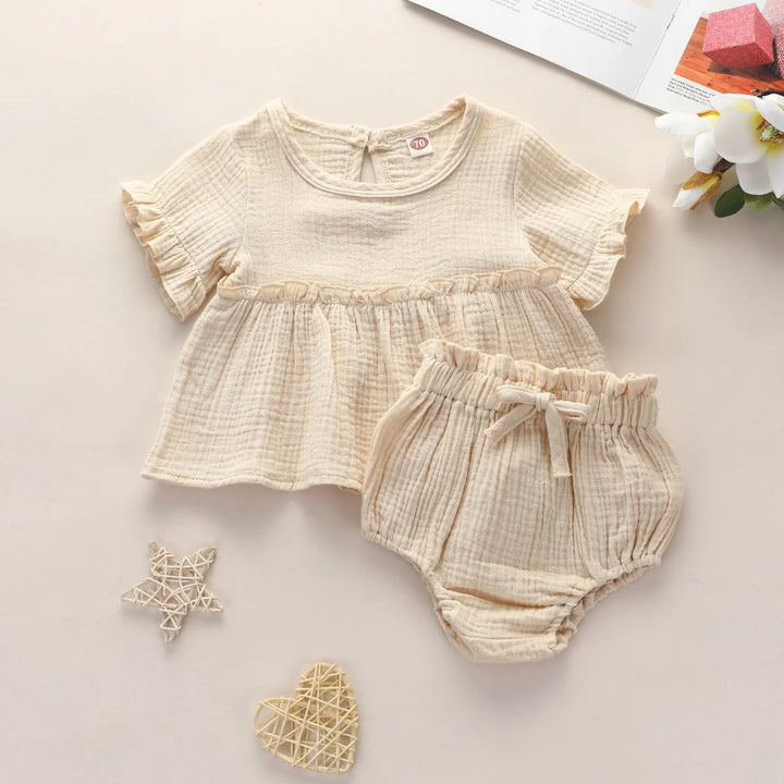 Beige baby outfit with top and bloomers on a light background