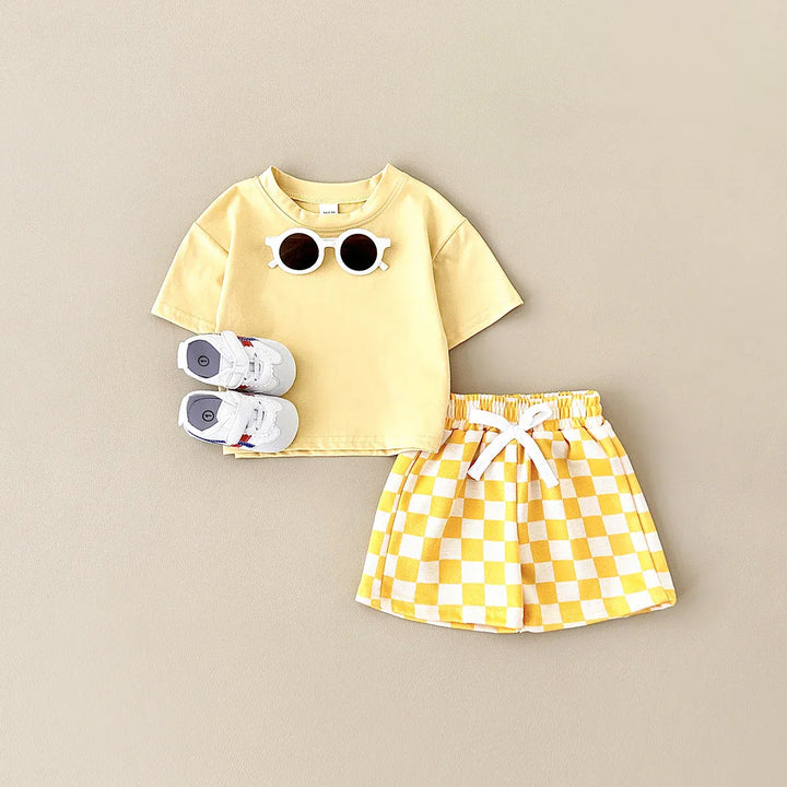 Yellow t-shirt with sunglasses design and checkered shorts on a beige background