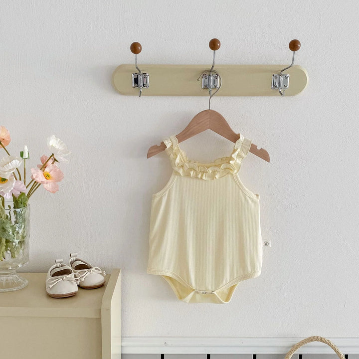 Yellow baby bodysuit on a hanger with a wall-mounted hook holder, flowers, and shoes in the background.