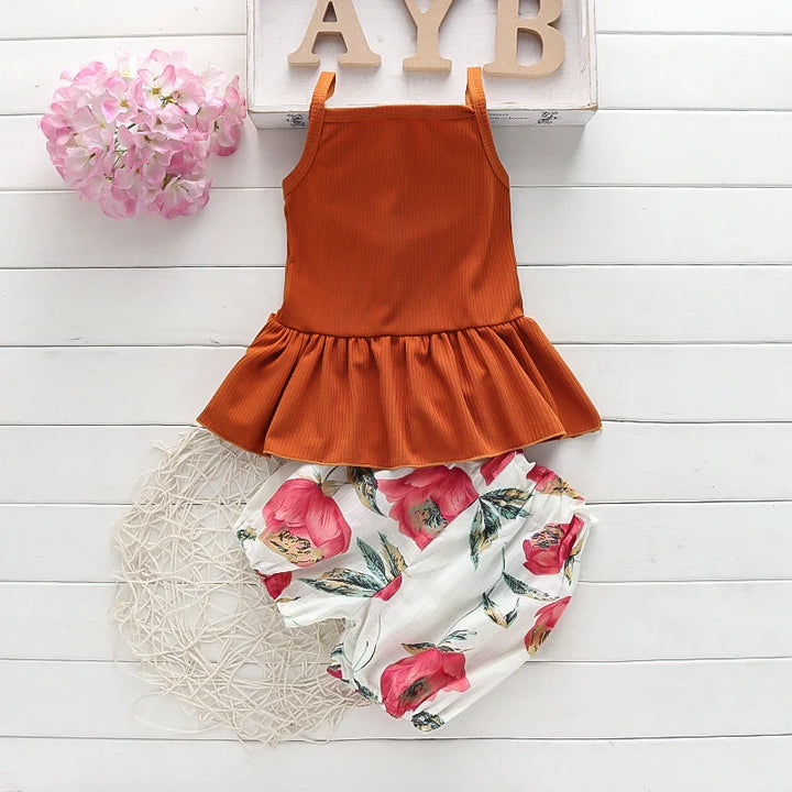Children's outfit with rust-colored top and floral shorts on a white wooden surface.