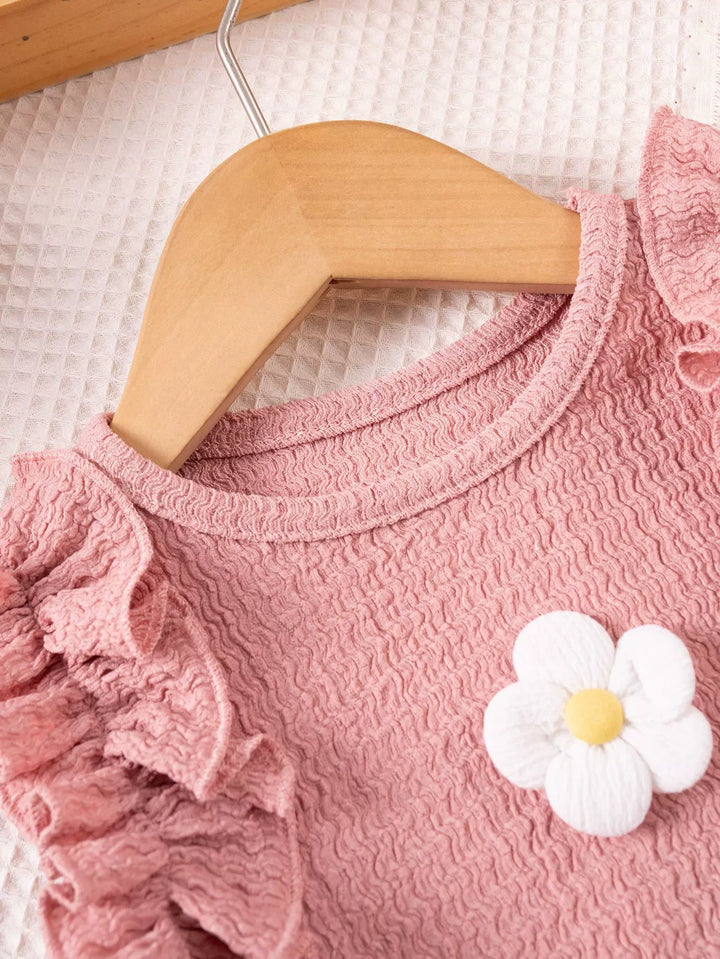 Pink textured garment with a white flower detail on a wooden hanger.