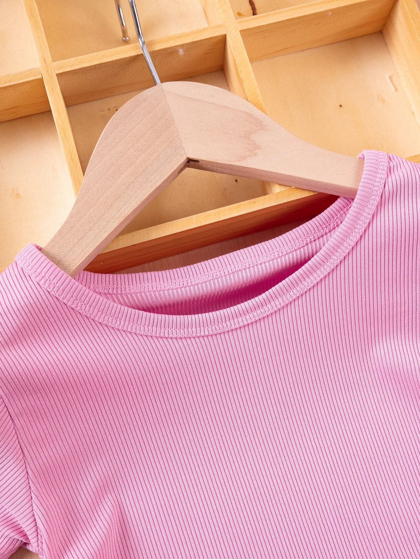 Pink t-shirt on a wooden hanger against a wooden background