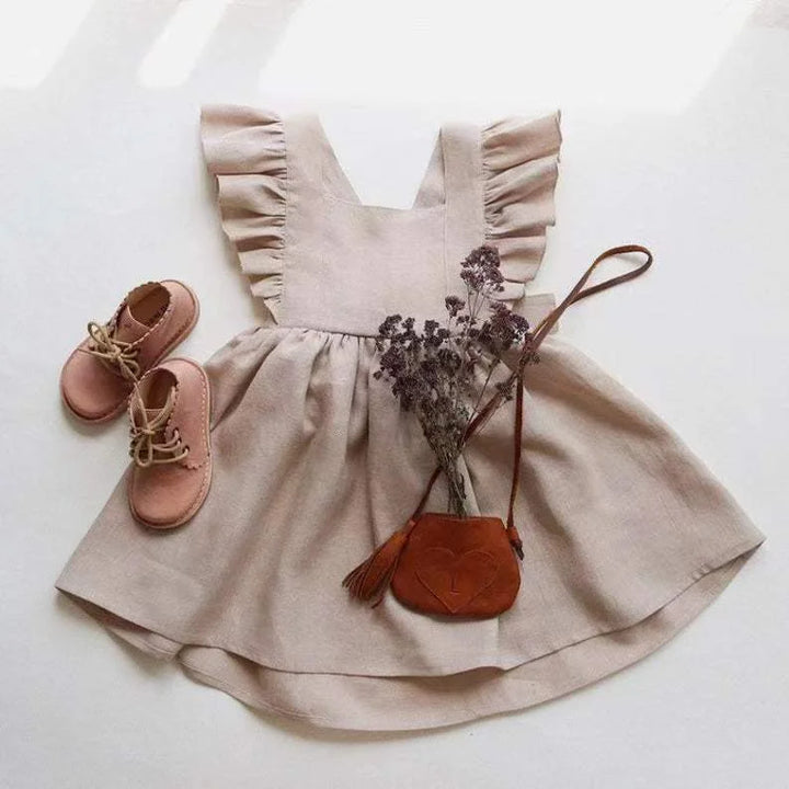 Beige dress with ruffled straps, pink shoes, and a small brown bag on a white background