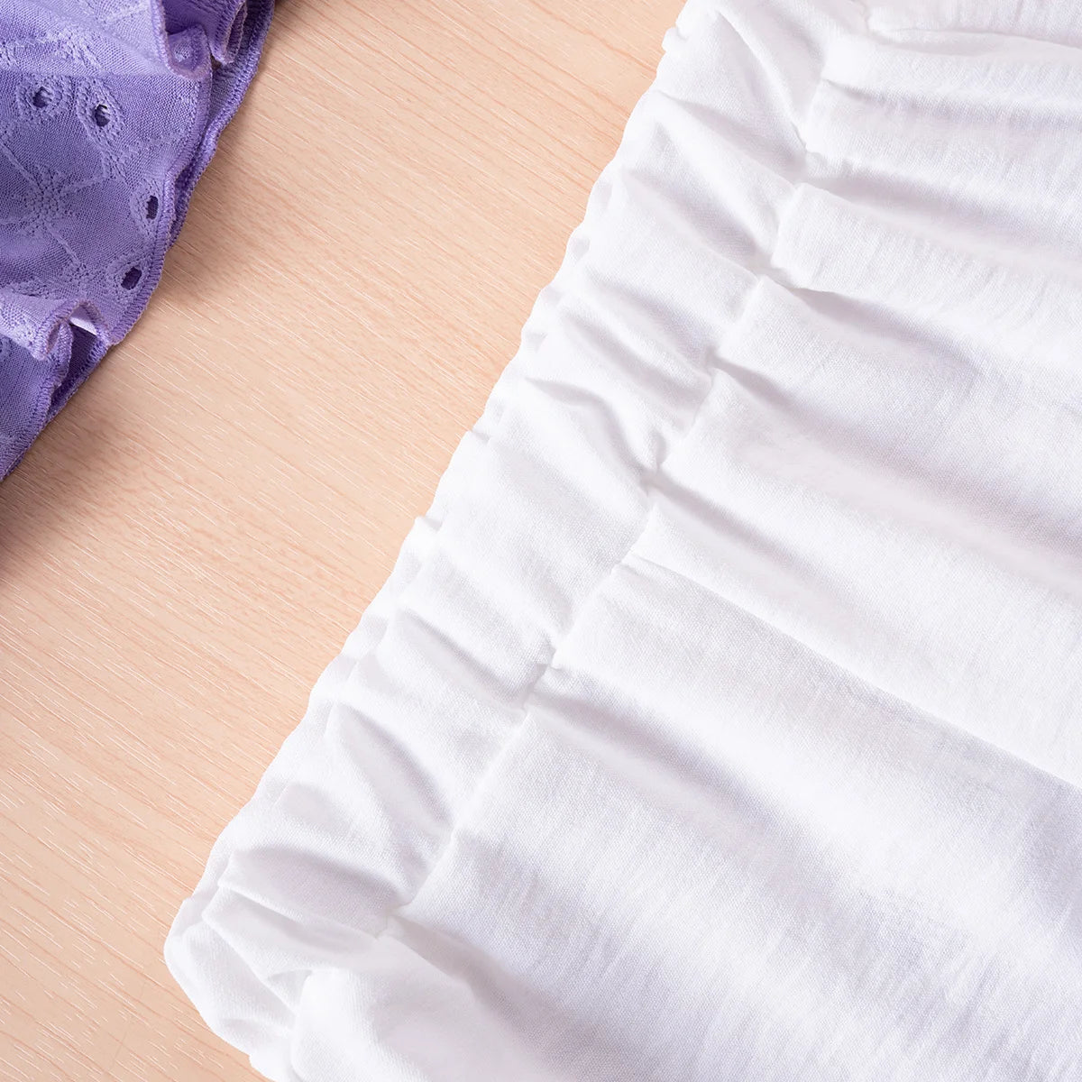 Close-up of white fabric with a purple textured item on a beige surface