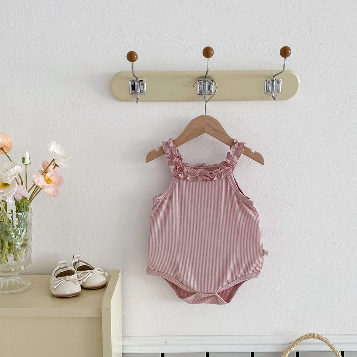 Pink baby romper on a hanger against a white wall with a small table and shoes in the foreground.