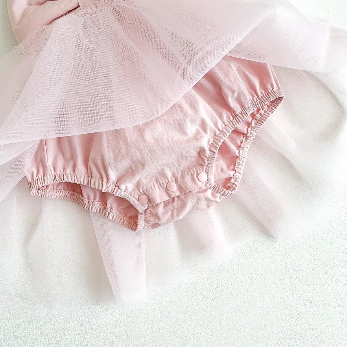 Pink baby bloomers with ruffled edges on a light background