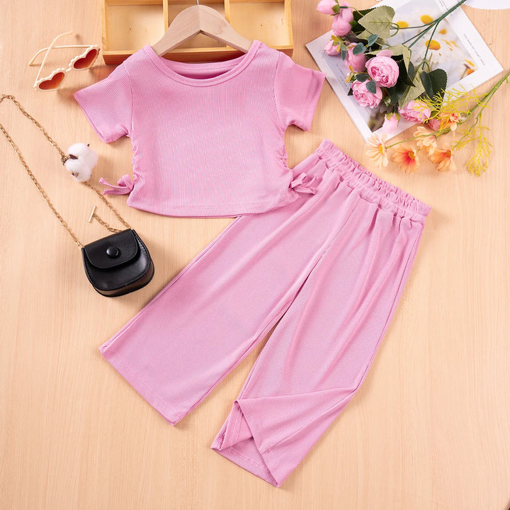 Pink outfit with top and pants on a wooden surface with accessories.