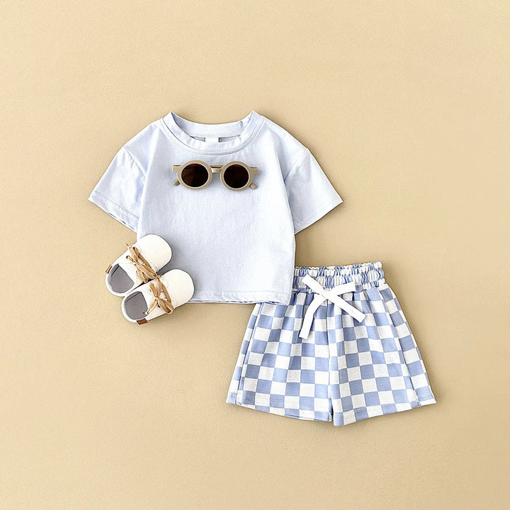 White t-shirt, checkered shorts, and baby shoes on a beige background