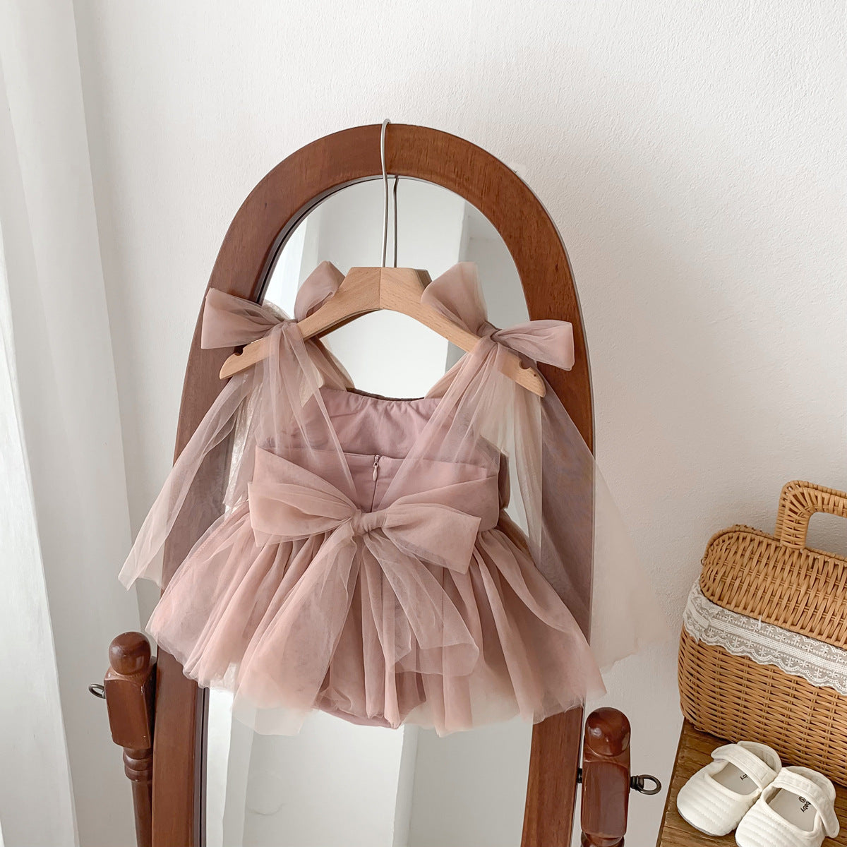 Pink children's dress with a large bow on a wooden hanger against a white wall.
