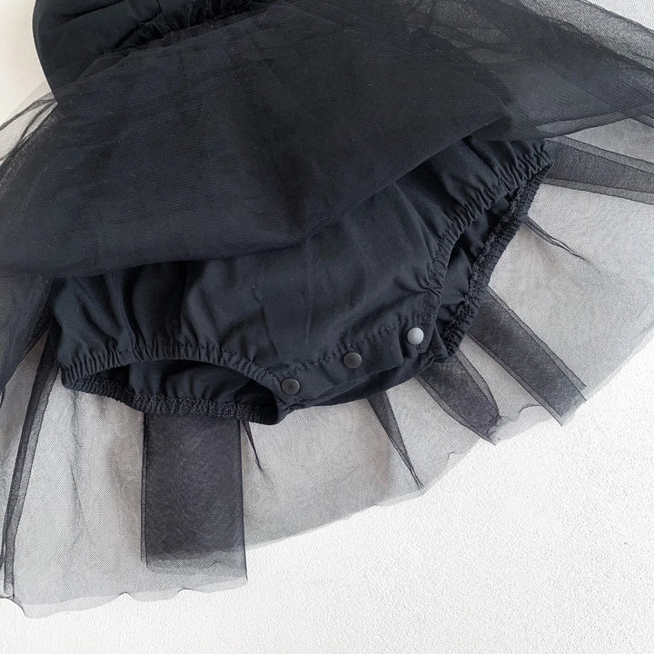 Black baby romper with sheer black tulle attached on a light gray background