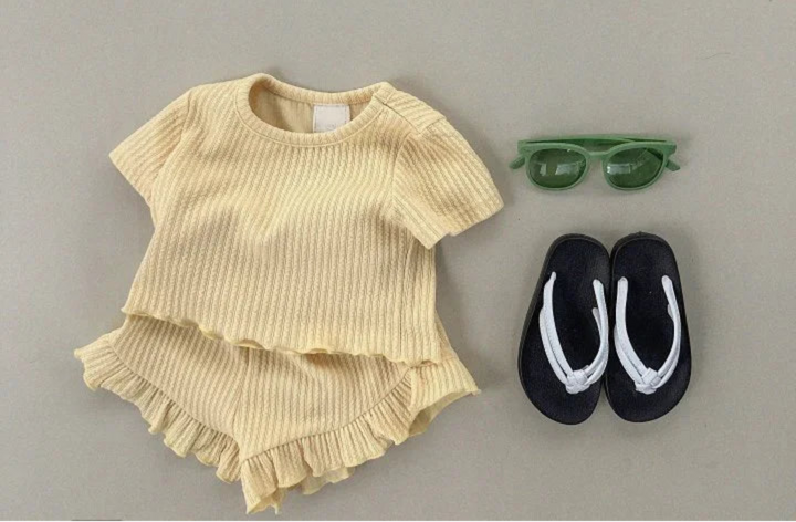 Yellow ruffled outfit with black sandals and green sunglasses on a gray background