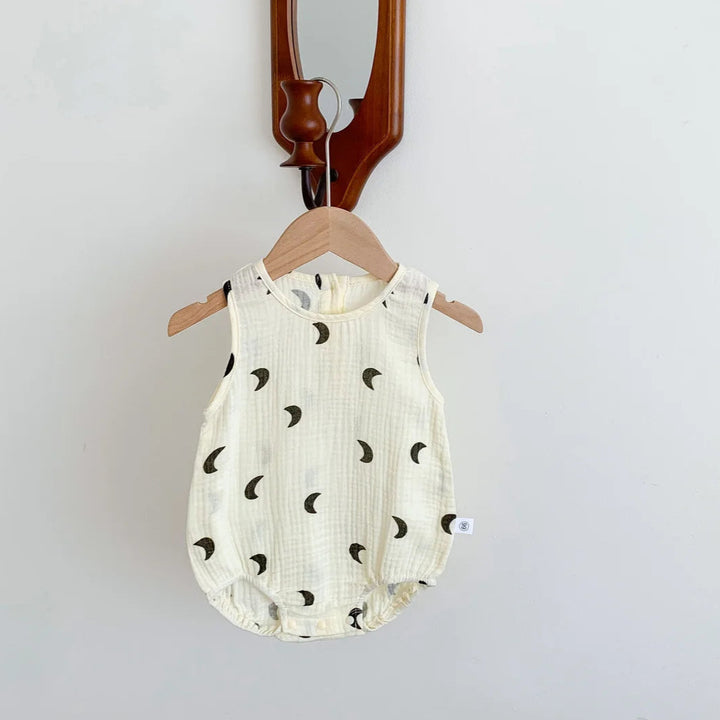 Baby romper with black moon pattern on a wooden hanger against a white wall.
