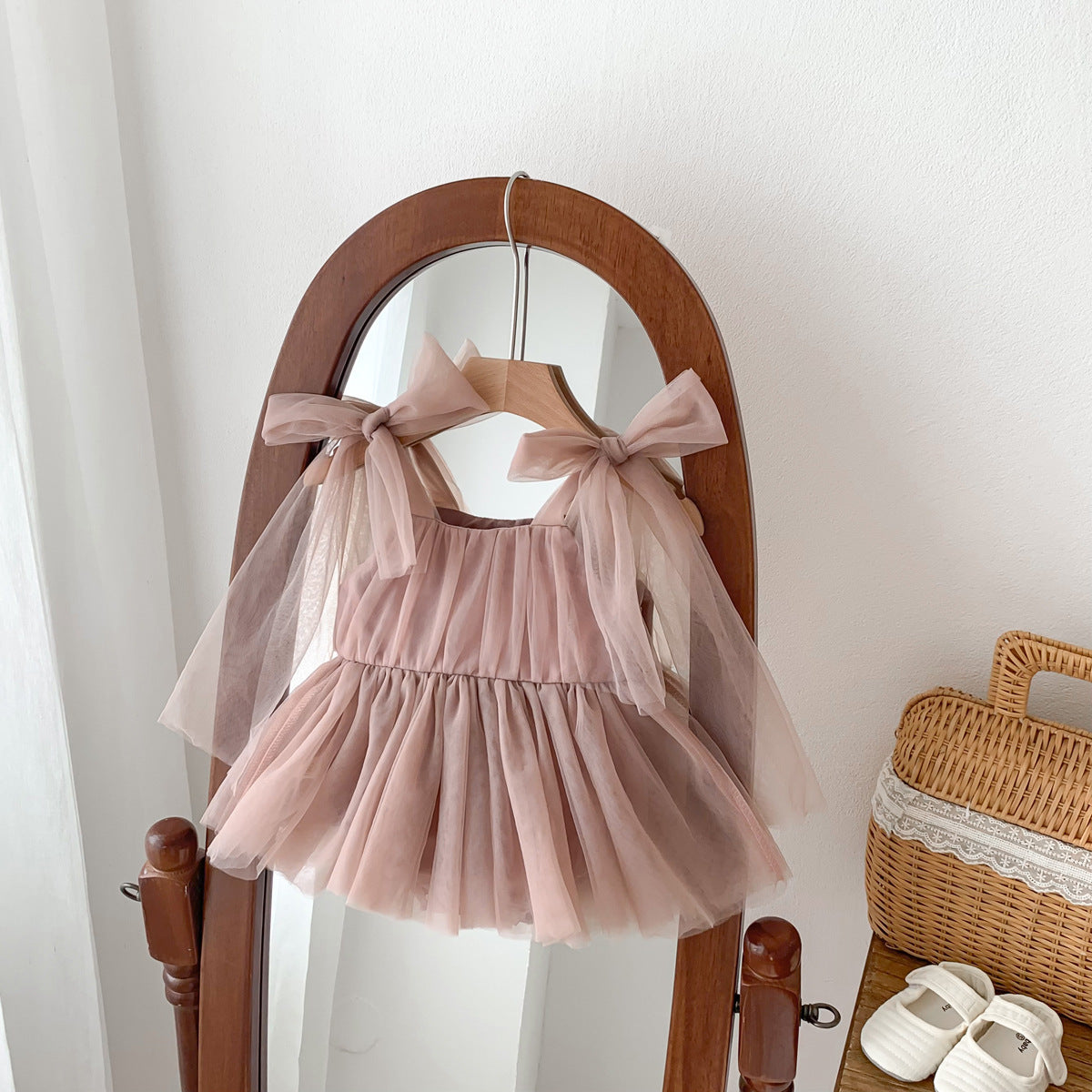 Pink children's dress with tulle layers on a wooden hanger against a white wall.