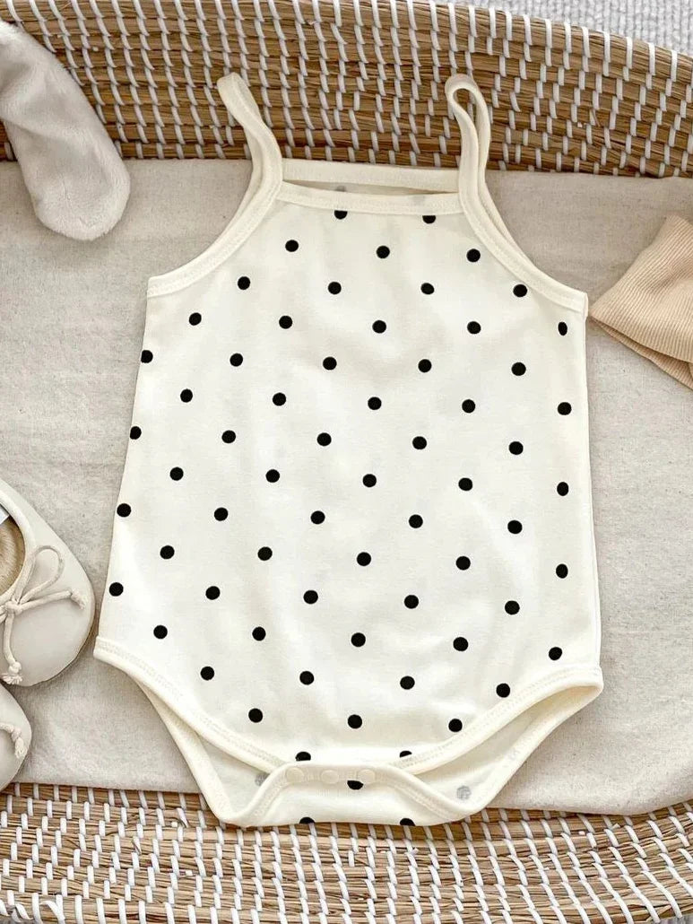White baby onesie with black polka dots on a textured surface