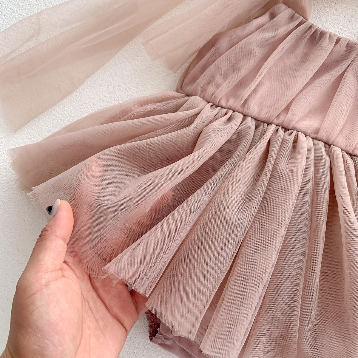 Close-up of a pink tulle skirt held by a hand on a light background