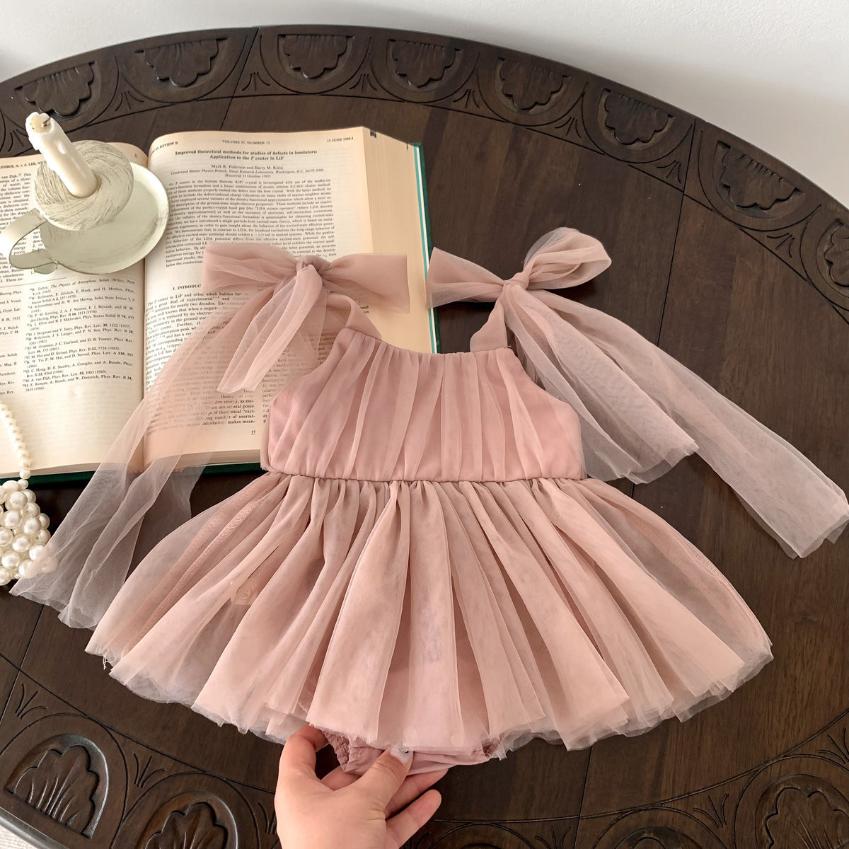 Pink tulle dress on a wooden table with an open book and decorative items.