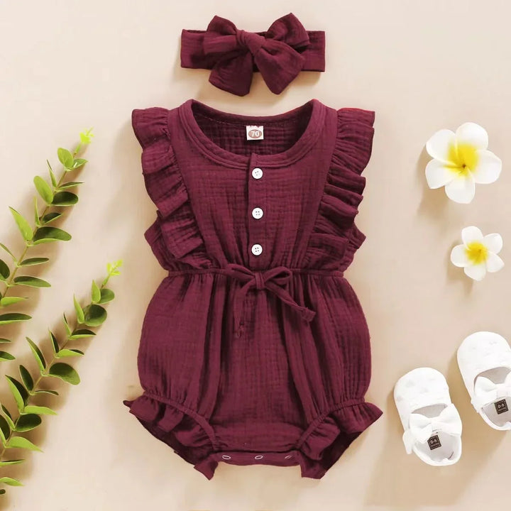 Maroon baby romper with ruffles, matching headband, and white shoes on a beige background.