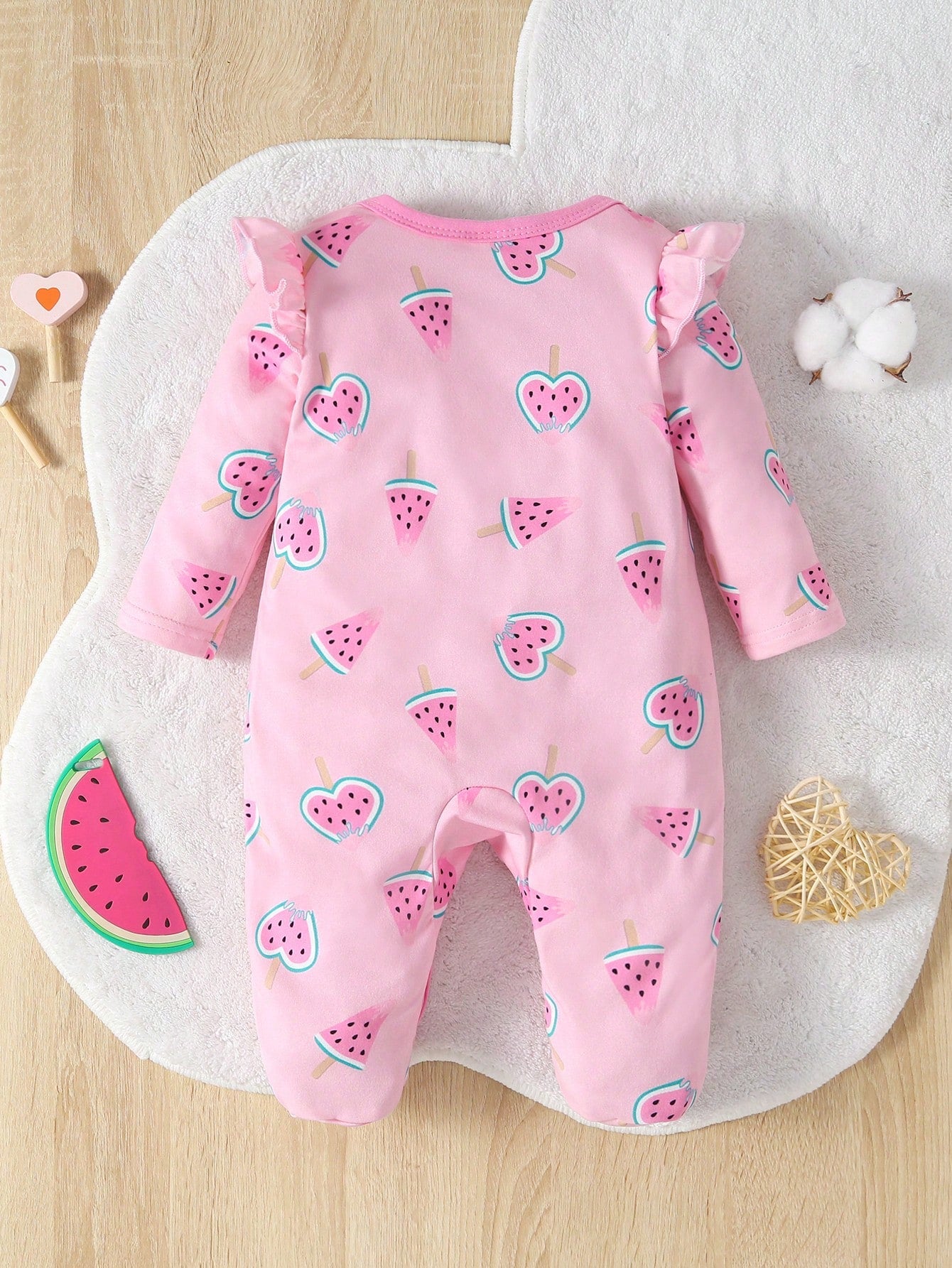 Pink baby onesie with watermelon pattern on a white mat
