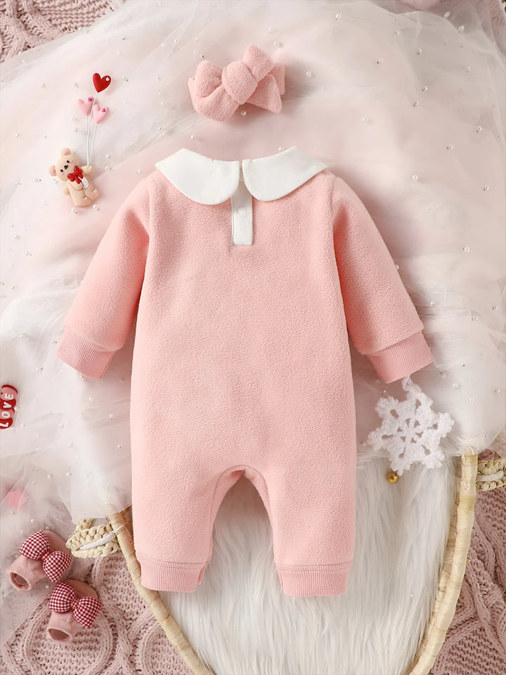 Pink baby romper with white collar on a soft, textured surface