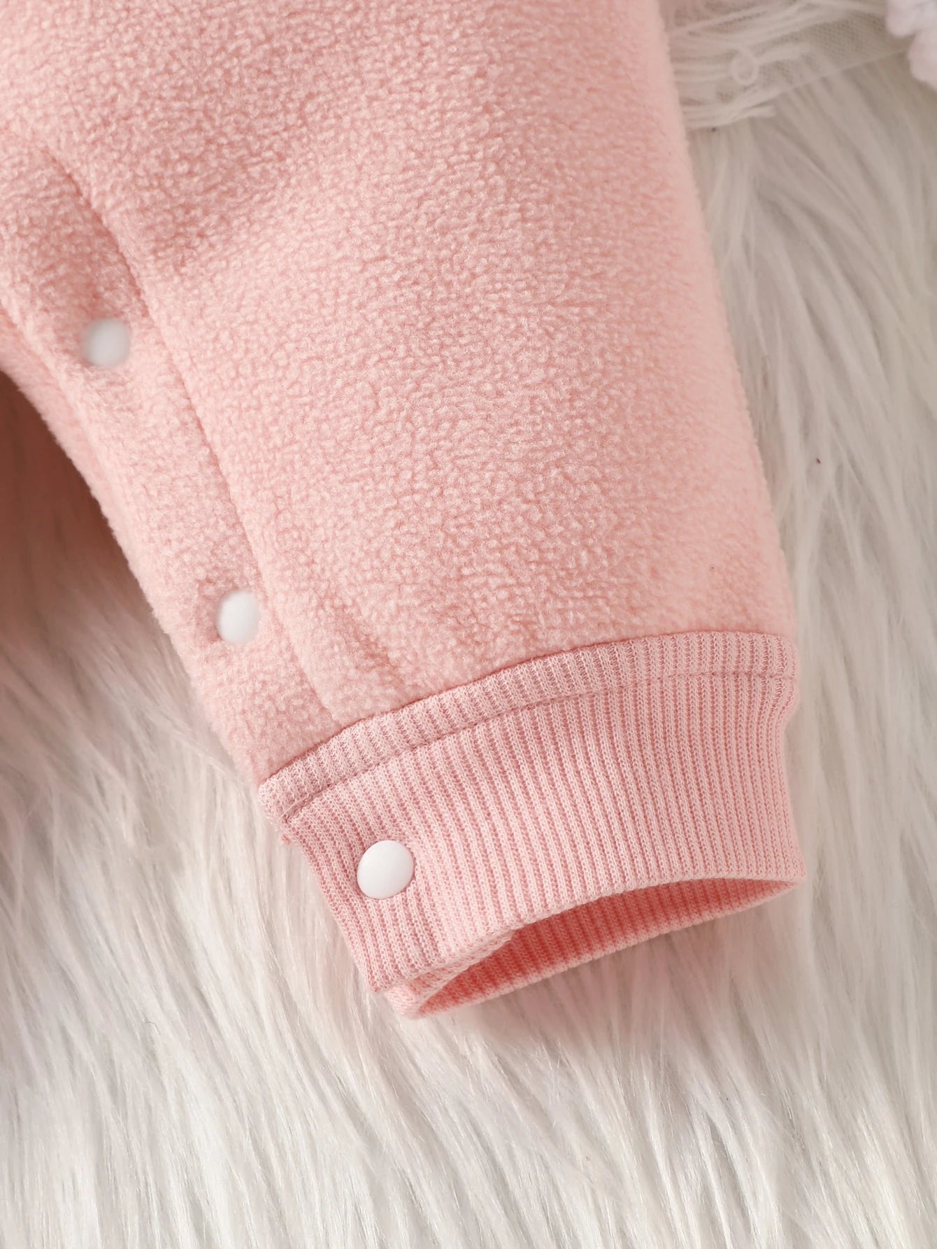 Close-up of a pink fleece jacket with white buttons on a fluffy white background