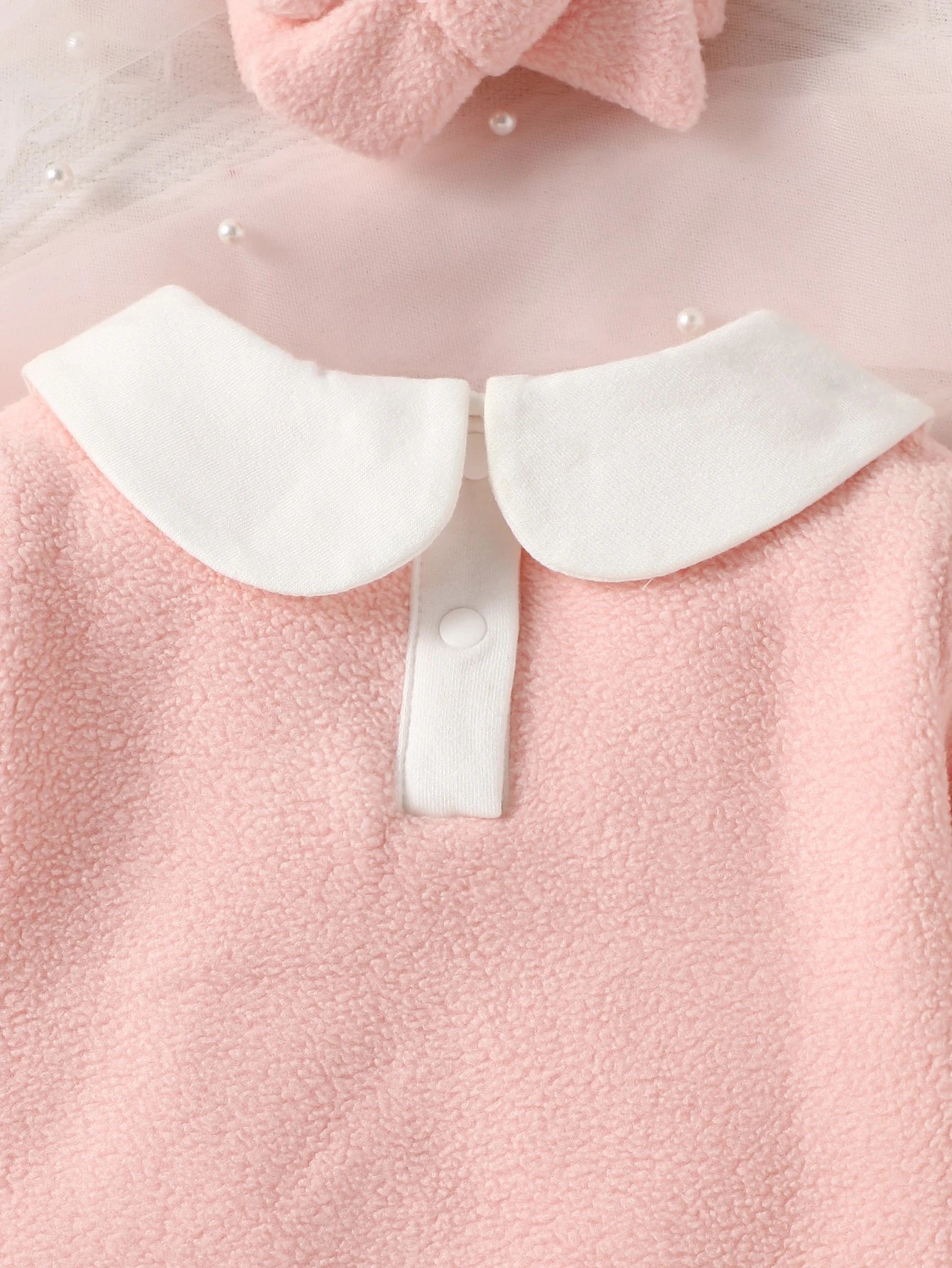 Close-up of a pink garment with a white collar and buttons.