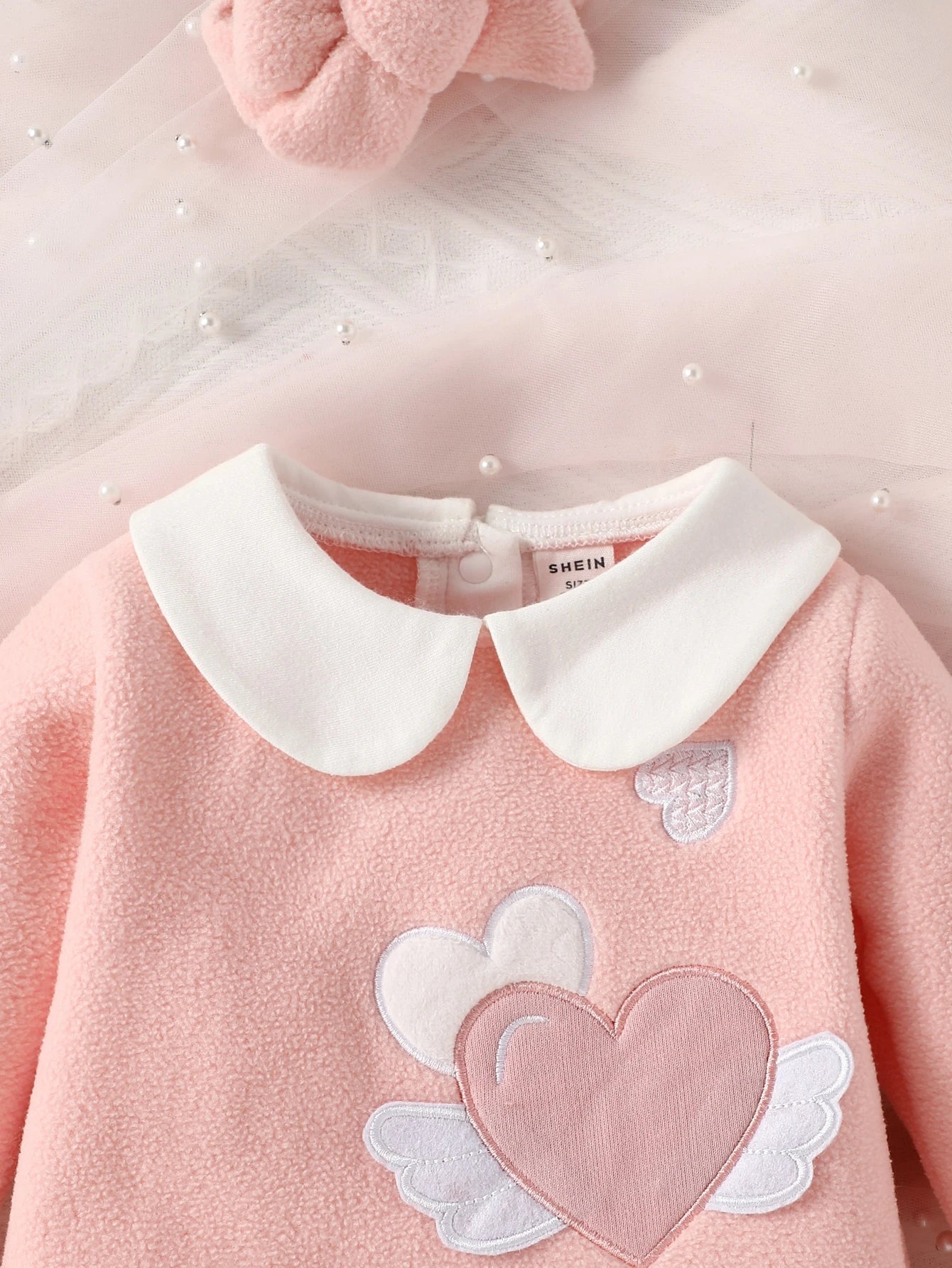 Pink sweater with white collar and heart design on a light pink background