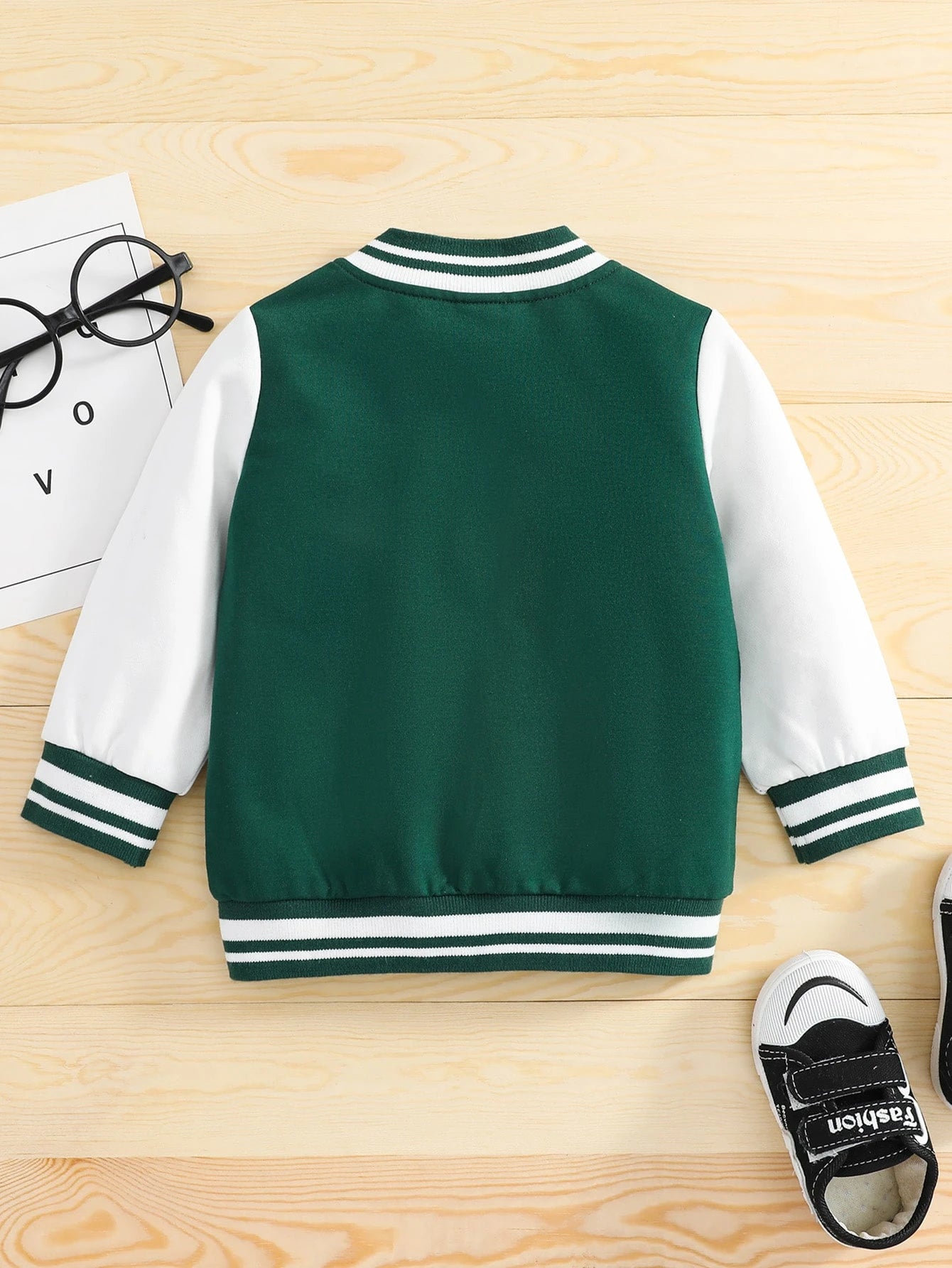 Green and white varsity jacket on a wooden surface with glasses and a shoe in the background.