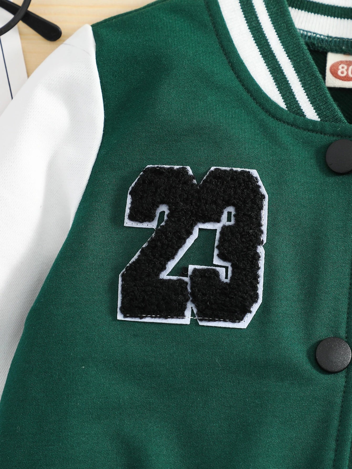 Green varsity jacket with number 23 patch on a light wooden surface