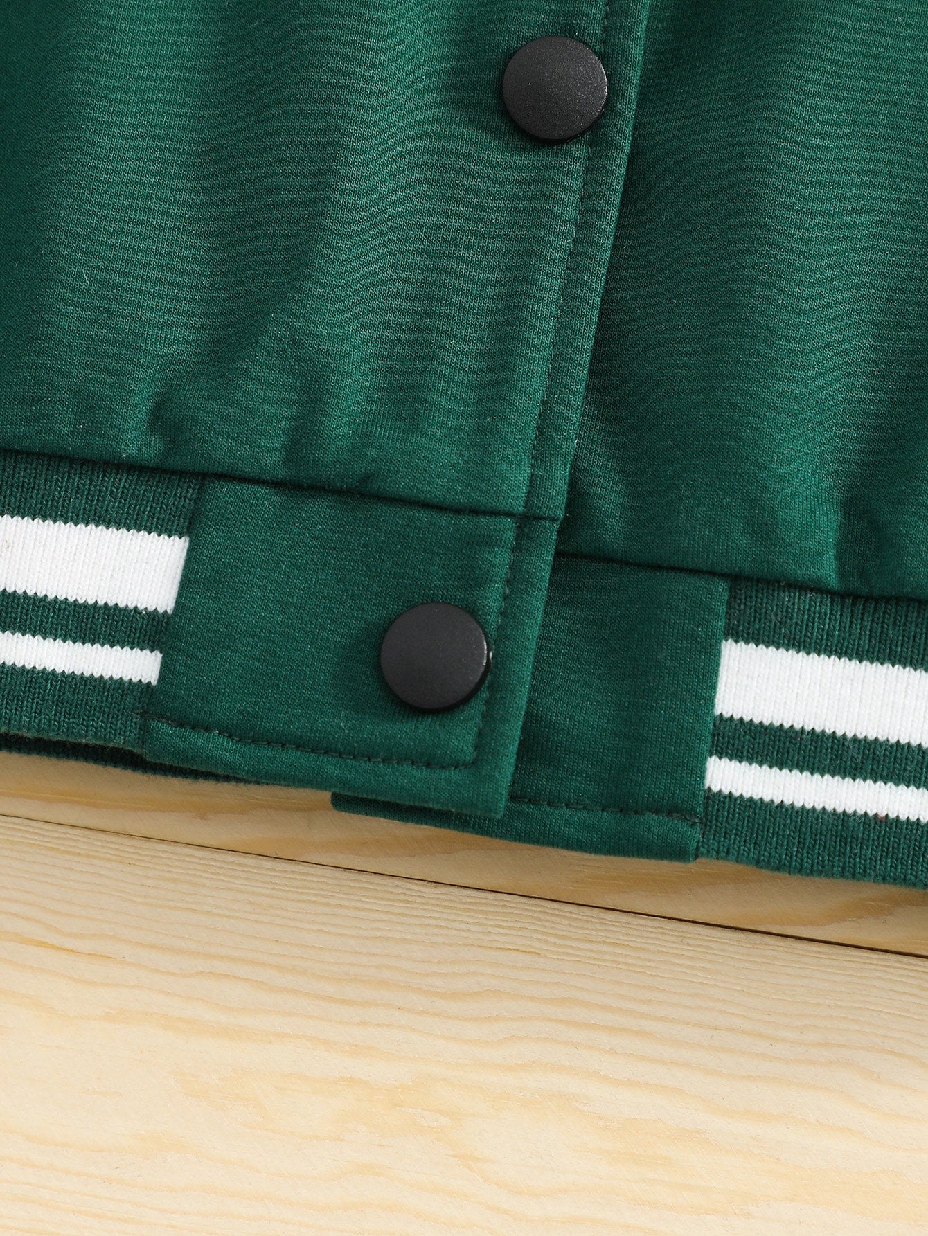 Green jacket with black buttons and white stripes on a wooden surface